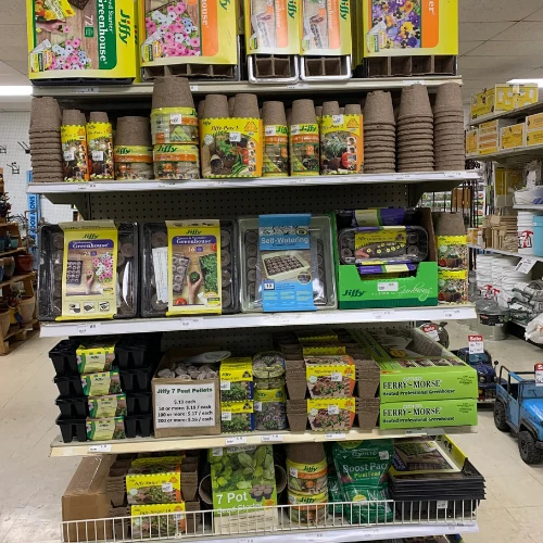 Garden center shelf stocked with Jiffy seed-starting kits, peat pots, planters, soil pellets, and colorful gardening supplies in an organized display.
