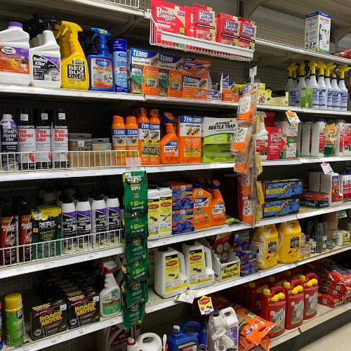 Retail store shelves display colorful household cleaning products, sprays, detergents, pest-control items, and beetle traps in neat rows.
